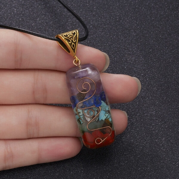 A rectangular orgonite pendant featuring layered chakra stones and a copper spiral encased in clear resin with an ornate brass bail.