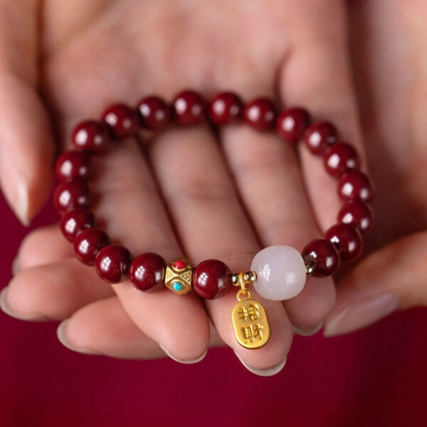 A string of deep red cinnabar beads featuring a luminous white stone and a dangling gold wealth amulet with Chinese characters.