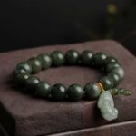 Polished dark green jade beads strung together with a carved light green Pixiu charm and gold accent thread.