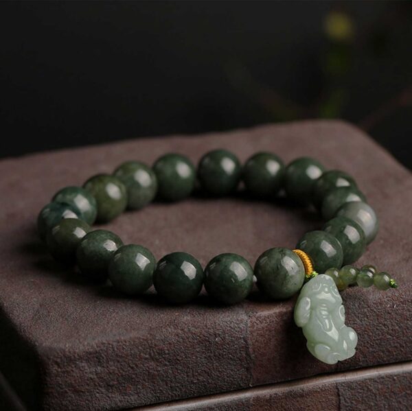 Polished dark green jade beads strung together with a carved light green Pixiu charm and gold accent thread.