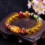 This vibrant bracelet features dominant golden-yellow citrine beads accented by red, green, black, and clear crystals representing the five elements, centered around an engraved wealth cylinder.