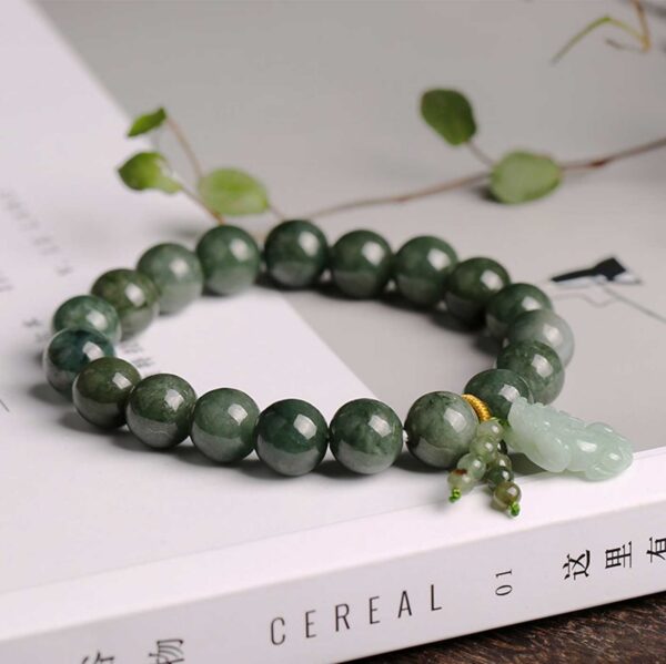 Polished dark green jade beads strung together with a carved light green Pixiu charm and gold accent thread.