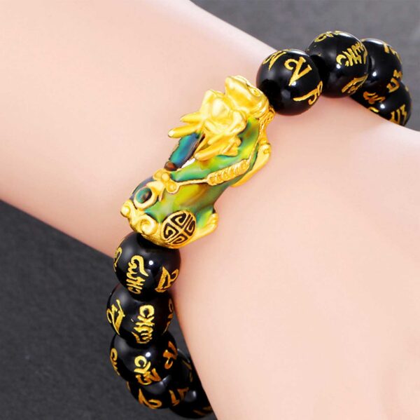 A striking bracelet featuring glossy black obsidian beads inscribed with golden Tibetan mantras, centered by an ornate gold and blue enamel Pixiu charm.