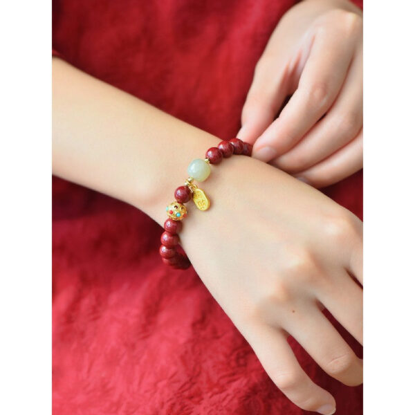 A string of deep red cinnabar beads featuring a luminous white stone and a dangling gold wealth amulet with Chinese characters.
