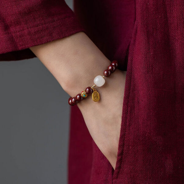 A string of deep red cinnabar beads featuring a luminous white stone and a dangling gold wealth amulet with Chinese characters.