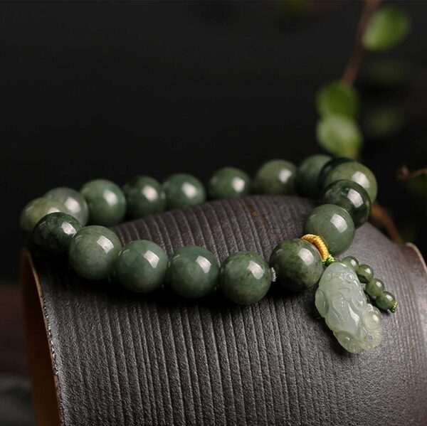 Polished dark green jade beads strung together with a carved light green Pixiu charm and gold accent thread.