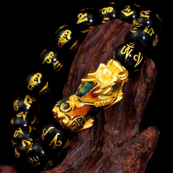 A striking bracelet featuring glossy black obsidian beads inscribed with golden Tibetan mantras, centered by an ornate gold and blue enamel Pixiu charm.