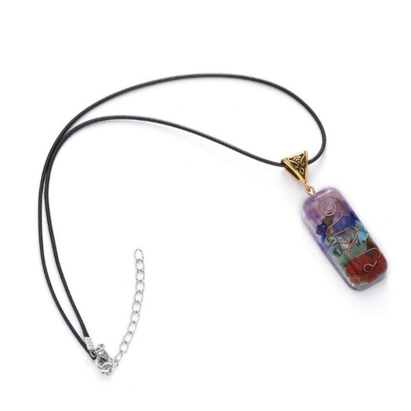 A rectangular orgonite pendant featuring layered chakra stones and a copper spiral encased in clear resin with an ornate brass bail.
