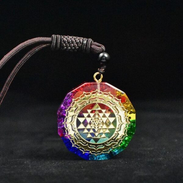 A vibrant rainbow-colored orgonite pendant featuring a gold Sri Yantra symbol suspended on a dark braided cord.