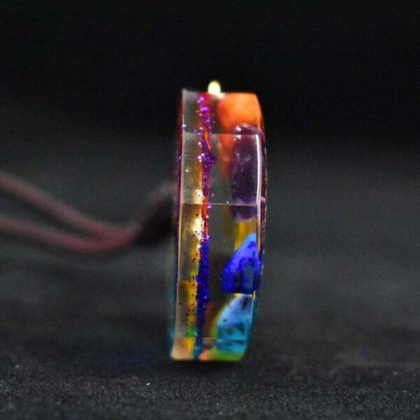 A vibrant rainbow-colored orgonite pendant featuring a gold Sri Yantra symbol suspended on a dark braided cord.