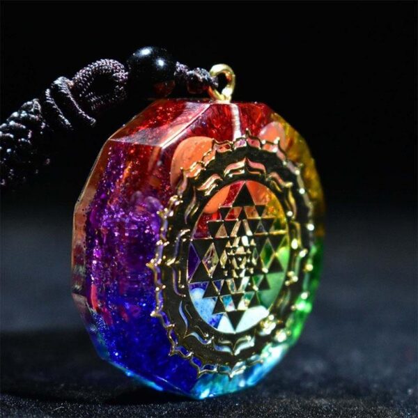 A vibrant rainbow-colored orgonite pendant featuring a gold Sri Yantra symbol suspended on a dark braided cord.