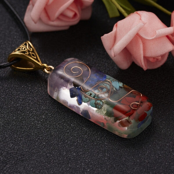 A rectangular orgonite pendant featuring layered chakra stones and a copper spiral encased in clear resin with an ornate brass bail.
