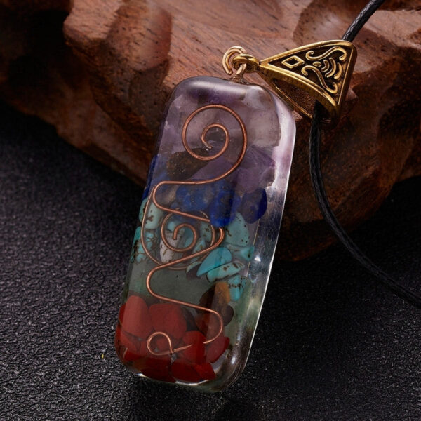 A rectangular orgonite pendant featuring layered chakra stones and a copper spiral encased in clear resin with an ornate brass bail.