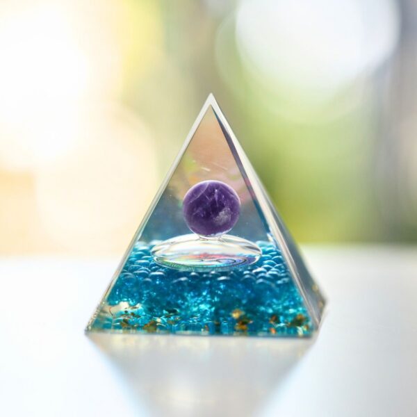 A translucent teal resin pyramid embedded with gold flakes and a central purple amethyst sphere marked with an Om symbol.