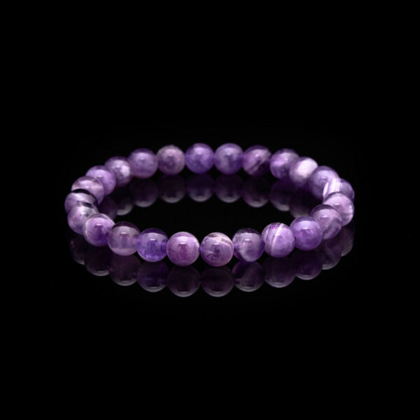 Polished round beads of deep violet amethyst are strung together to form a simple yet elegant bracelet resting on a natural fabric background.