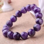 Polished round beads of deep violet amethyst are strung together to form a simple yet elegant bracelet resting on a natural fabric background.