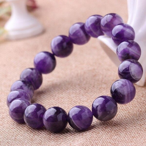 Polished round beads of deep violet amethyst are strung together to form a simple yet elegant bracelet resting on a natural fabric background.