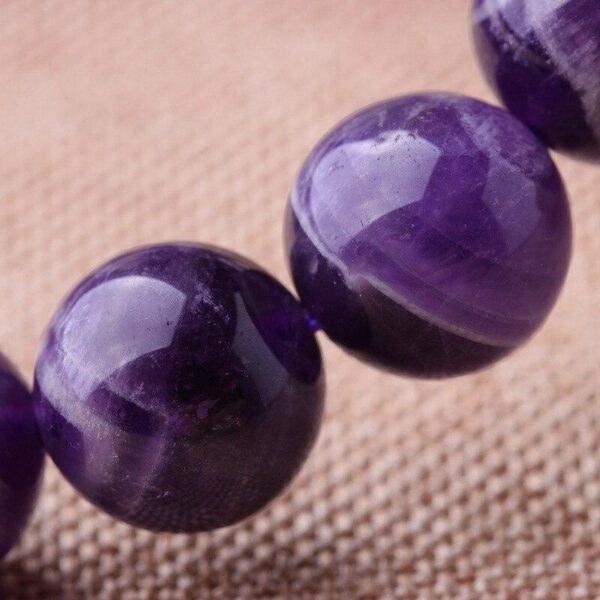 Polished round beads of deep violet amethyst are strung together to form a simple yet elegant bracelet resting on a natural fabric background.