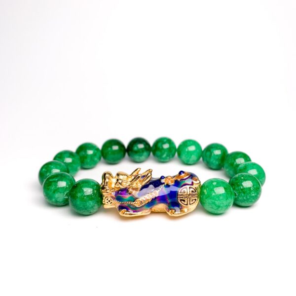 Vibrant green jade beads encircle a striking gold and blue enamel Pixiu charm set against a rustic wooden background.