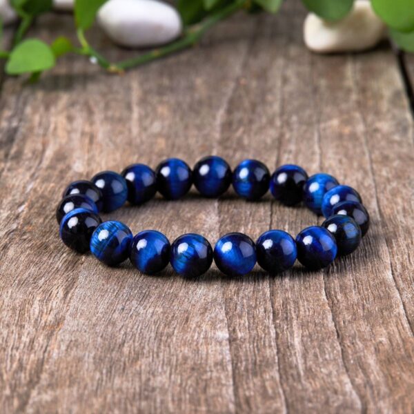 Polished round beads of deep blue Tiger's Eye with striking chatoyancy rest on a textured monochrome surface.