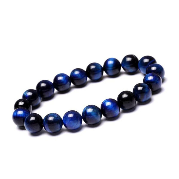 Polished round beads of deep blue Tiger's Eye with striking chatoyancy rest on a textured monochrome surface.