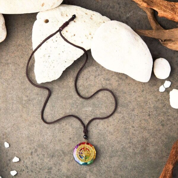 A vibrant rainbow-colored orgonite pendant featuring a gold Sri Yantra symbol suspended on a dark braided cord.