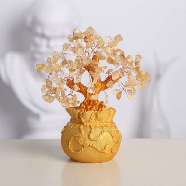 A handcrafted wire tree adorned with raw citrine chips sits atop a textured golden money bag base against a black background.