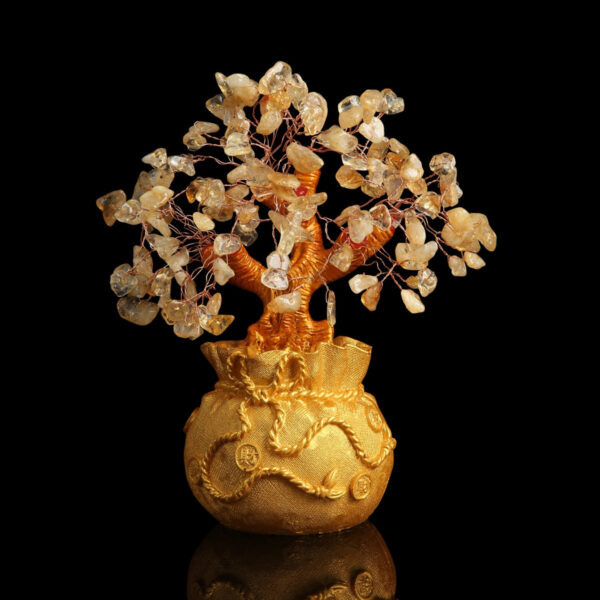 A handcrafted wire tree adorned with raw citrine chips sits atop a textured golden money bag base against a black background.