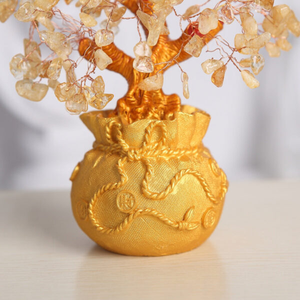 A handcrafted wire tree adorned with raw citrine chips sits atop a textured golden money bag base against a black background.