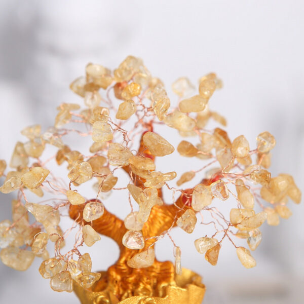 A handcrafted wire tree adorned with raw citrine chips sits atop a textured golden money bag base against a black background.