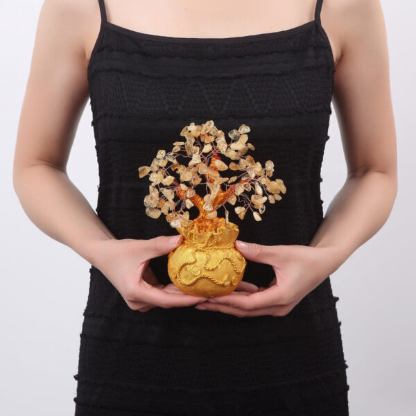 A handcrafted wire tree adorned with raw citrine chips sits atop a textured golden money bag base against a black background.