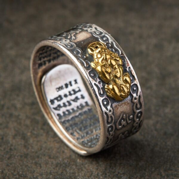 A striking silver-toned band featuring a detailed gold Pixiu creature surrounded by geometric patterns and sacred mantra engravings on the interior.