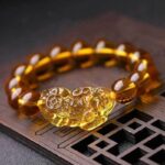 A luminous bracelet featuring translucent golden citrine beads centered around an intricately carved Pixiu charm resting on a dark wooden surface.