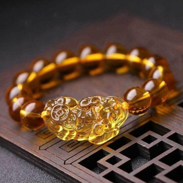 A luminous bracelet featuring translucent golden citrine beads centered around an intricately carved Pixiu charm resting on a dark wooden surface.