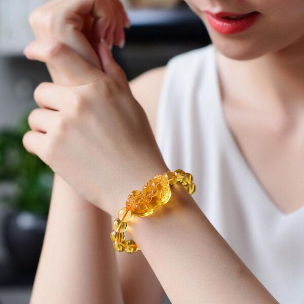 A luminous bracelet featuring translucent golden citrine beads centered around an intricately carved Pixiu charm resting on a dark wooden surface.