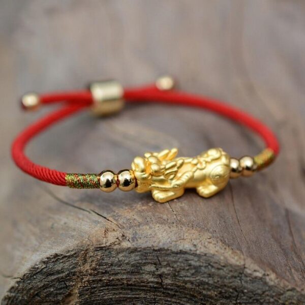 A lustrous gold Pixiu charm centered on a vibrant red braided cord with adjustable gold beads and sliding knot closure.