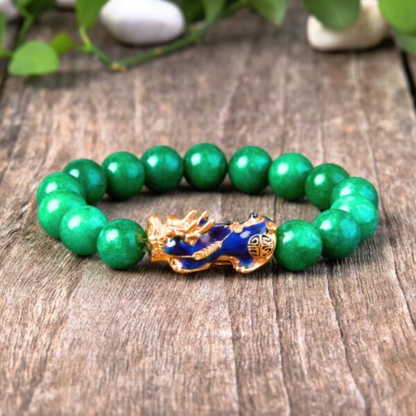 Vibrant green jade beads encircle a striking gold and blue enamel Pixiu charm set against a rustic wooden background.