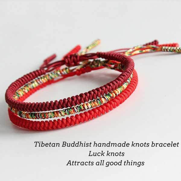 Three intricately braided rope bracelets in vibrant red, deep maroon, and multi-colored threads featuring adjustable sliding knots against a natural wood background.