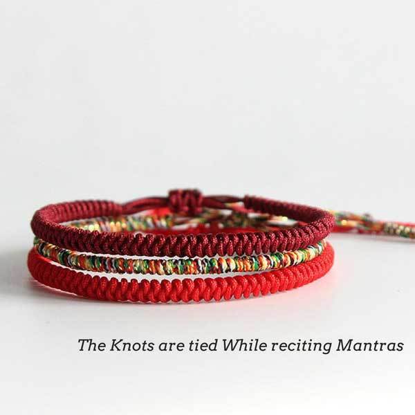 Three intricately braided rope bracelets in vibrant red, deep maroon, and multi-colored threads featuring adjustable sliding knots against a natural wood background.