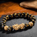 Glossy black obsidian beads engraved with golden mantras are centered by a detailed gold Pixiu beast and coin charms.
