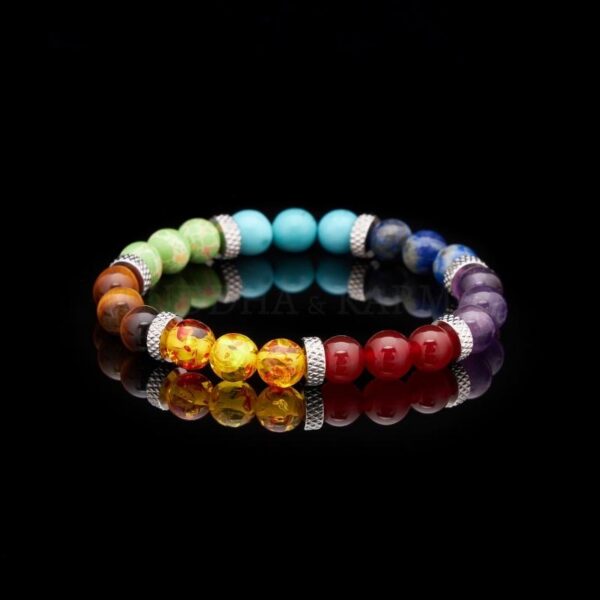 A colorful beaded bracelet showcasing seven distinct gemstone hues separated by textured silver spacers on a rustic wood background.