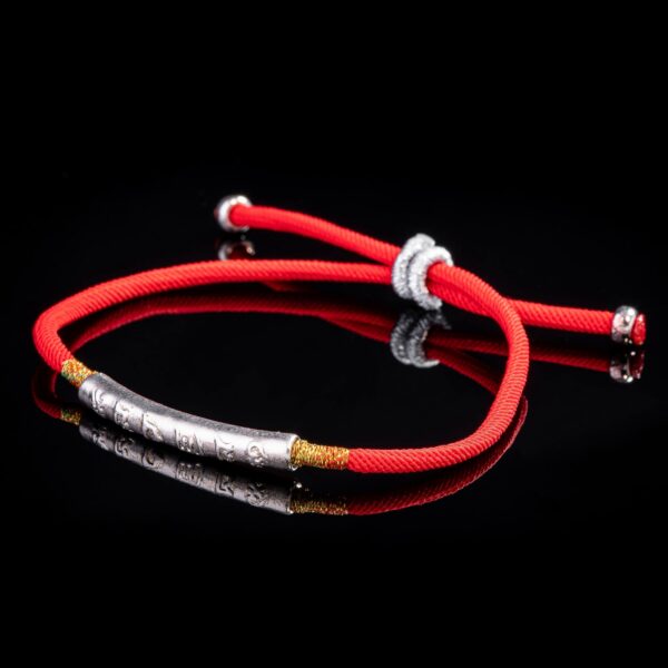 A vibrant red braided cord bracelet featuring an engraved gold-tone cylindrical bead and adjustable sliding knots.