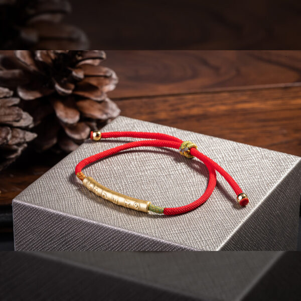 A vibrant red braided cord bracelet featuring an engraved gold-tone cylindrical bead and adjustable sliding knots.