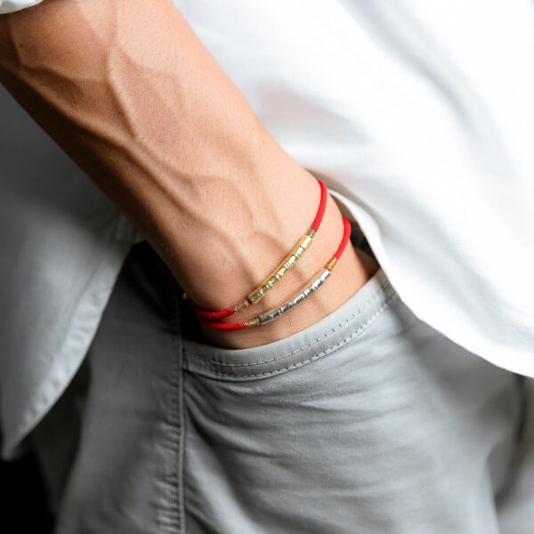 A vibrant red braided cord bracelet featuring an engraved gold-tone cylindrical bead and adjustable sliding knots.