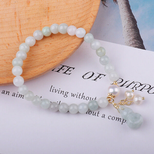 Featuring smooth light green jade beads, this bracelet is elegantly detailed with white pearls and a traditional Wu Lou gourd charm on gold accents.