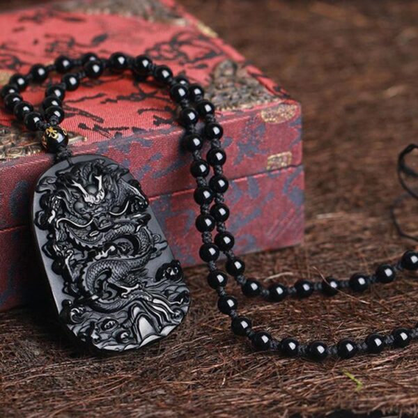 A glossy black obsidian pendant featuring an intricately carved Chinese dragon relief suspended on a matching bead necklace.