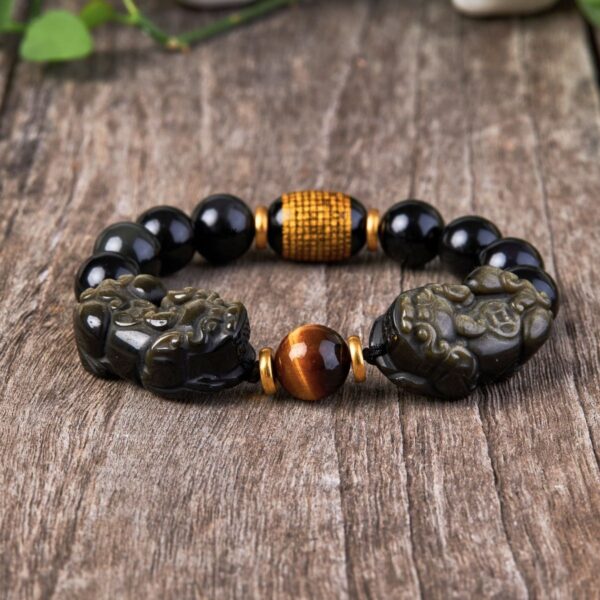 Glossy black obsidian beads with golden sheen threaded alongside two detailed metallic Pixiu charms.