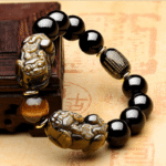 Glossy black obsidian beads with golden sheen threaded alongside two detailed metallic Pixiu charms.