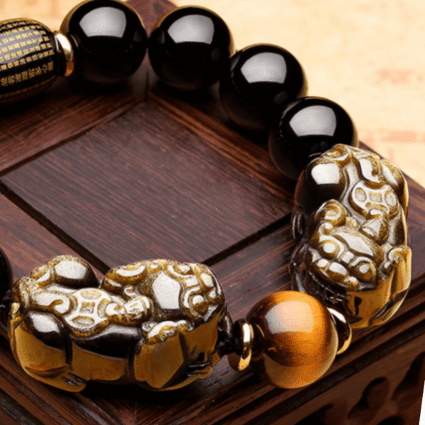 Glossy black obsidian beads with golden sheen threaded alongside two detailed metallic Pixiu charms.