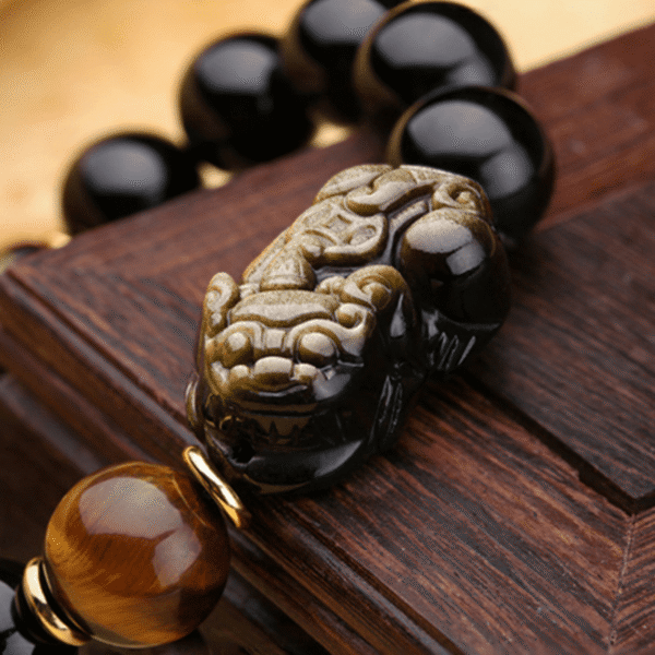 Glossy black obsidian beads with golden sheen threaded alongside two detailed metallic Pixiu charms.